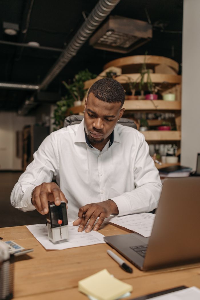 A professional adult stamping documents at a desk with a laptop in an office setting.